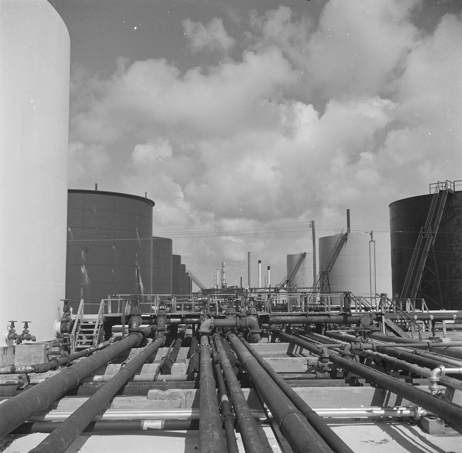 Storage tanks and a long alley of pipework at the Lago refinery, San Nicolas, Aruba, in 1947, under a sky of cumulus cloud