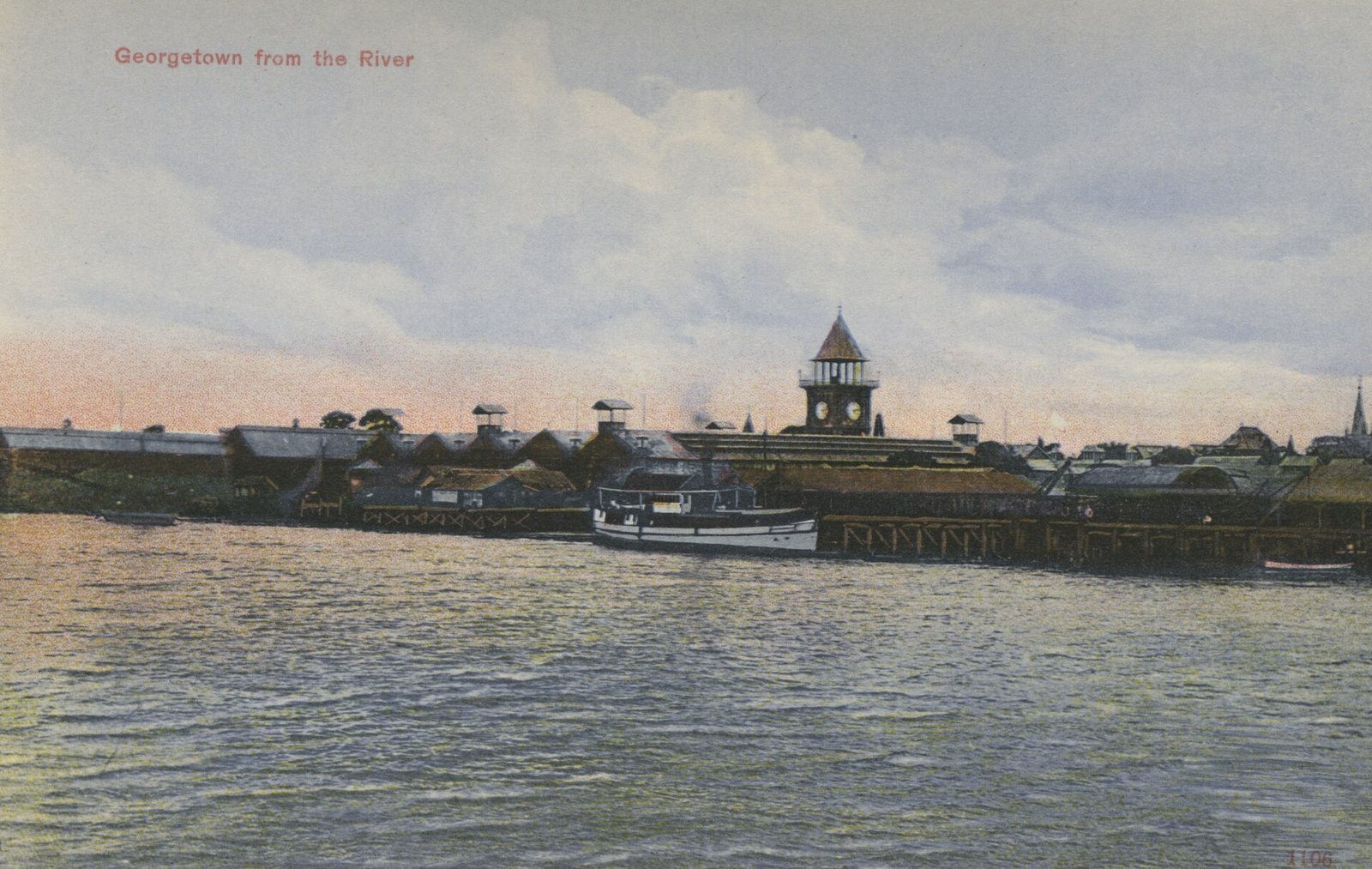 Georgetown seen from the Demerara River around 1910: the stellings and waterfront sheds, a steam launch, and the Stabroek Market clock tower rising at the centre