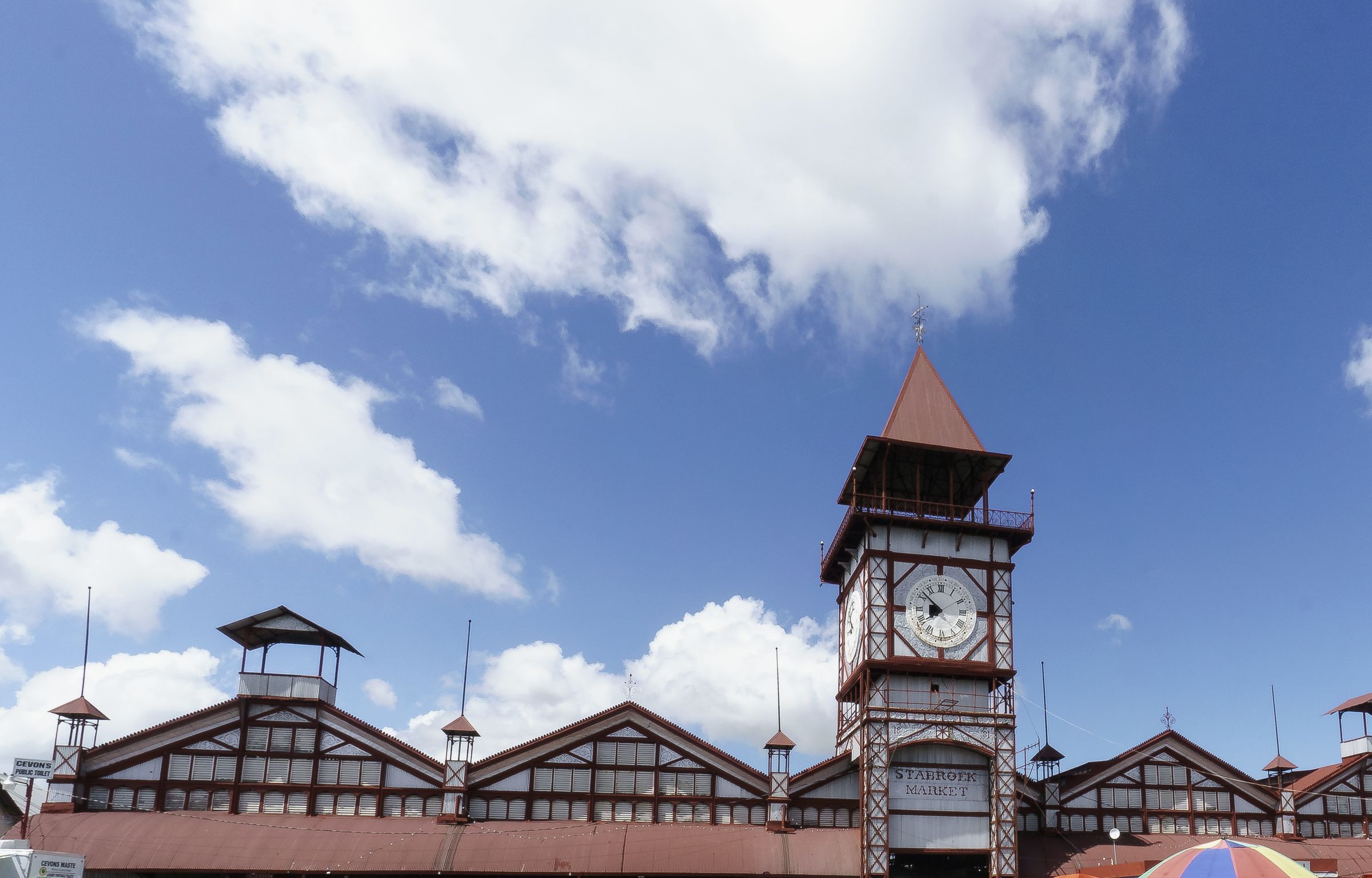 The clock tower and iron roofs of Stabroek Market, Georgetown, under a blue sky.